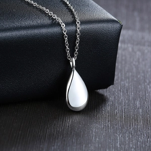 Polished silver teardrop urn pendant hanging on a luxury black leather jewelry box edge