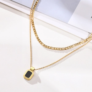 Detail of layered gold necklace with rectangular black pendant and dual chain textures