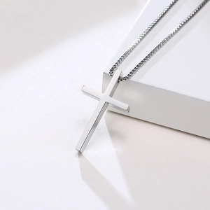 Macro side view of silver stainless steel cross pendant and durable box chain on white pedestal