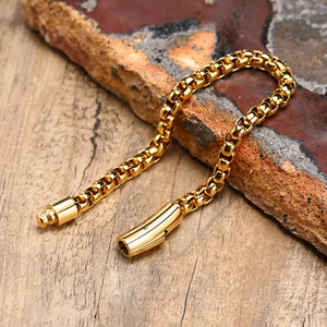 Detail of golden box chain bracelet with cylinder clasp on dark rock and wood background
