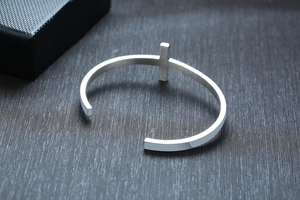 Detailed view of silver stainless steel open bangle featuring a 3D cross motif on a dark base