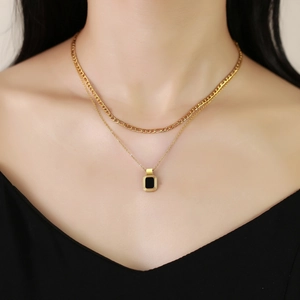 Close-up of golden double-layer necklace featuring a black rectangular geometric pendant