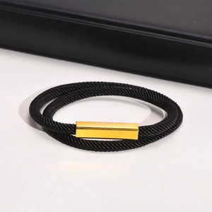 Detail of black woven rope bracelet featuring a polished gold rectangular metal charm