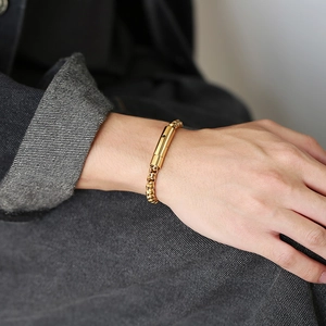 Detail of men's gold box chain bracelet with a cylindrical clasp worn on wrist