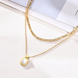 Detail of gold double-layered necklace with square pendant and Figaro chain on white background