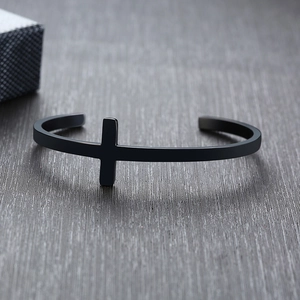 Macro detail of a black matte stainless steel cross cuff bracelet on a textured surface