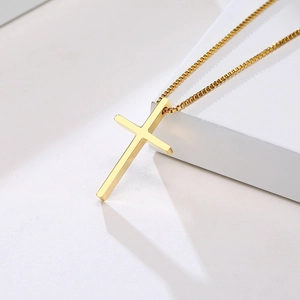 Macro shot of minimalist gold cross pendant and polished box chain on stone block