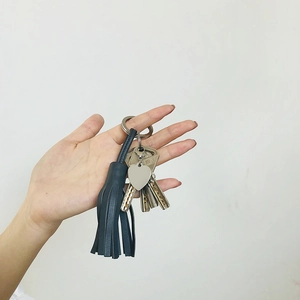Detail of dark blue leather tassel keychain with a heart pendant held by a hand