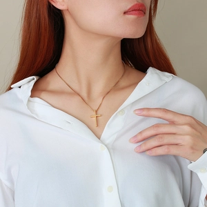 Close-up of a minimalist golden cross necklace worn on a white shirt with box chain detail