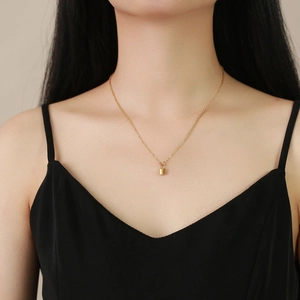 Close-up of golden padlock pendant necklace worn by a model on a minimalist chain