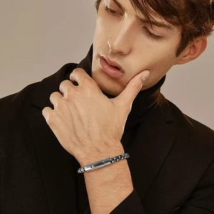 Detail view of men's silver box chain bracelet with a cylindrical clasp on wrist