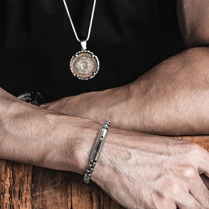 Close-up of stainless steel box chain bracelet and vintage coin pendant necklace on model