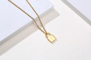 Close-up of golden padlock pendant necklace on white marble and minimalist background