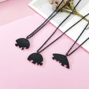 Dettaglio di tre collane puzzle a cuore in acciaio nero su uno sfondo rosa tenue