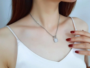 Detailed view of a silver stainless steel lock pendant necklace worn on a model's neck