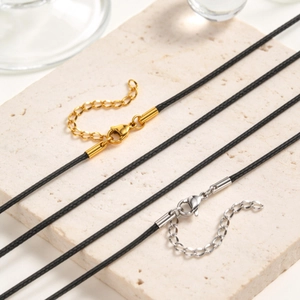 Close-up of black wax cord necklaces with gold and silver lobster clasps on stone