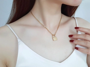 Polished gold padlock pendant necklace on woman wearing a white silk camisole