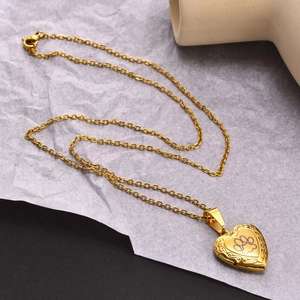Close-up of golden heart locket with black paw print and intricate floral engravings