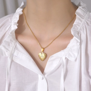 Detailed view of a gold heart locket necklace with a paw print worn by a model