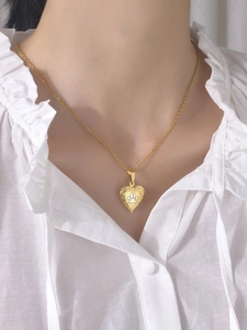 Close-up of golden heart locket necklace with paw print worn by model on white shirt