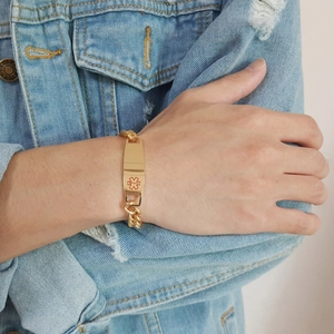 Détail d'un bracelet d'alerte médicale en acier doré porté au poignet d'un modèle