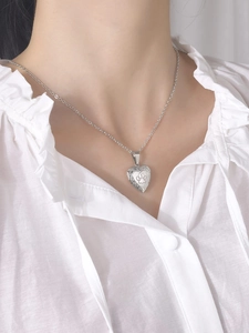 Close-up of heart-shaped steel locket necklace with paw print engraving on a model