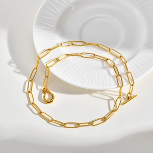 Detailed view of golden paperclip link necklace with toggle clasp on a white plate