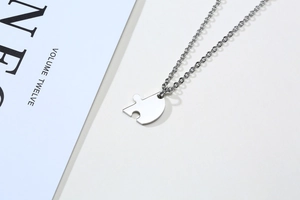 Close-up of polished stainless steel heart puzzle piece necklace on a clean white surface