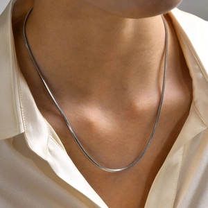 Dettaglio della sottile collana a catena a serpente argento indossata su seta beige