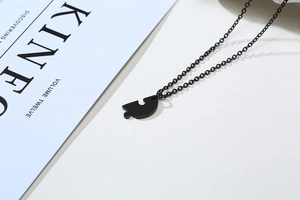 Macro detail of a matte black stainless steel heart puzzle necklace on a magazine background