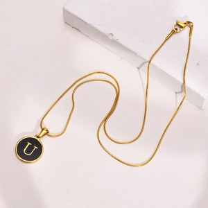 Detail shot of a gold initial U pendant necklace with a black enamel disc and snake chain