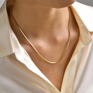 Primo piano di una collana a catena serpente quadrata dorata indossata con una camicia