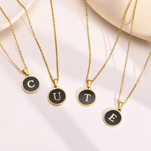 Detail of four golden letter necklaces forming the word CUTE with black enamel pendants