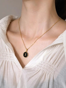 Close-up of golden necklace with circular black pendant featuring capital letter X