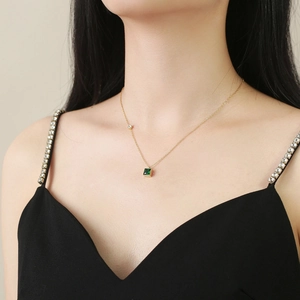Close-up of golden necklace featuring a square green zircon pendant worn by a model