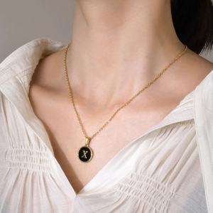 Elegant gold necklace with a round black pendant featuring a gold letter X design