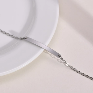 Close-up of polished stainless steel curved ID bar bracelet with delicate link chain