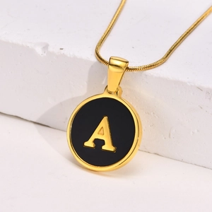 Detail of 18K gold letter A pendant with black enamel on a textured stone surface