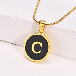 Detailed view of a gold initial C pendant on a delicate snake chain over a stone block