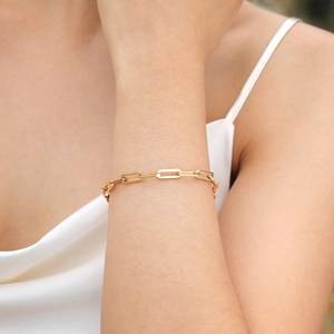 Detailed view of a gold paperclip link chain bracelet on a wrist with white silk fabric