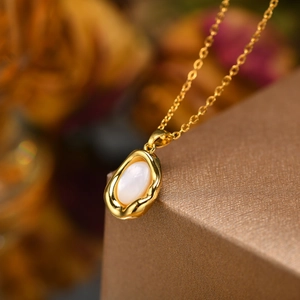 Macro detail of teardrop gold pendant with white shell inlay on a delicate cable chain