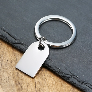 Close-up of polished stainless steel arched dog tag keychain on a stone and wood surface