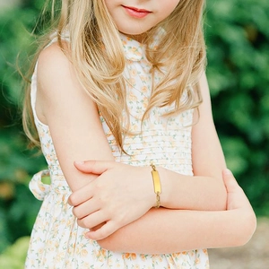 Custom engraved gold ID bracelet for kids on a girl's wrist in outdoor natural light