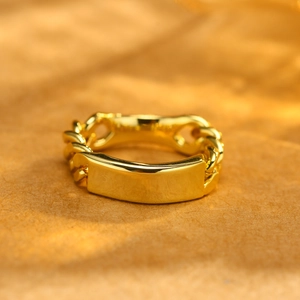 Macro detail of golden chain ring featuring a polished rectangular plate on textured surface