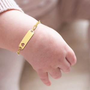 Detailed view of baby gold bracelet with hollow heart ID plate on infant wrist