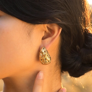 Boucles d'oreilles gouttes dorées texture tissée portées sous lumière naturelle