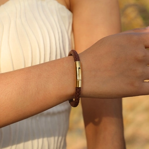 Gros plan d'un bracelet en cuir tressé marron avec fermoir métallique doré au poignet