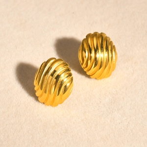 Macro shot of golden shell texture earrings with a ribbed circular finish on beige velvet