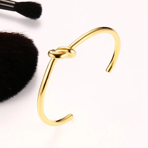 Detailed close-up of a golden titanium steel knotted cuff bracelet on a white background