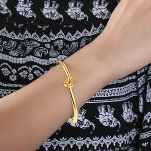 Detailed view of a gold-plated titanium steel knot cuff bracelet worn on a female wrist